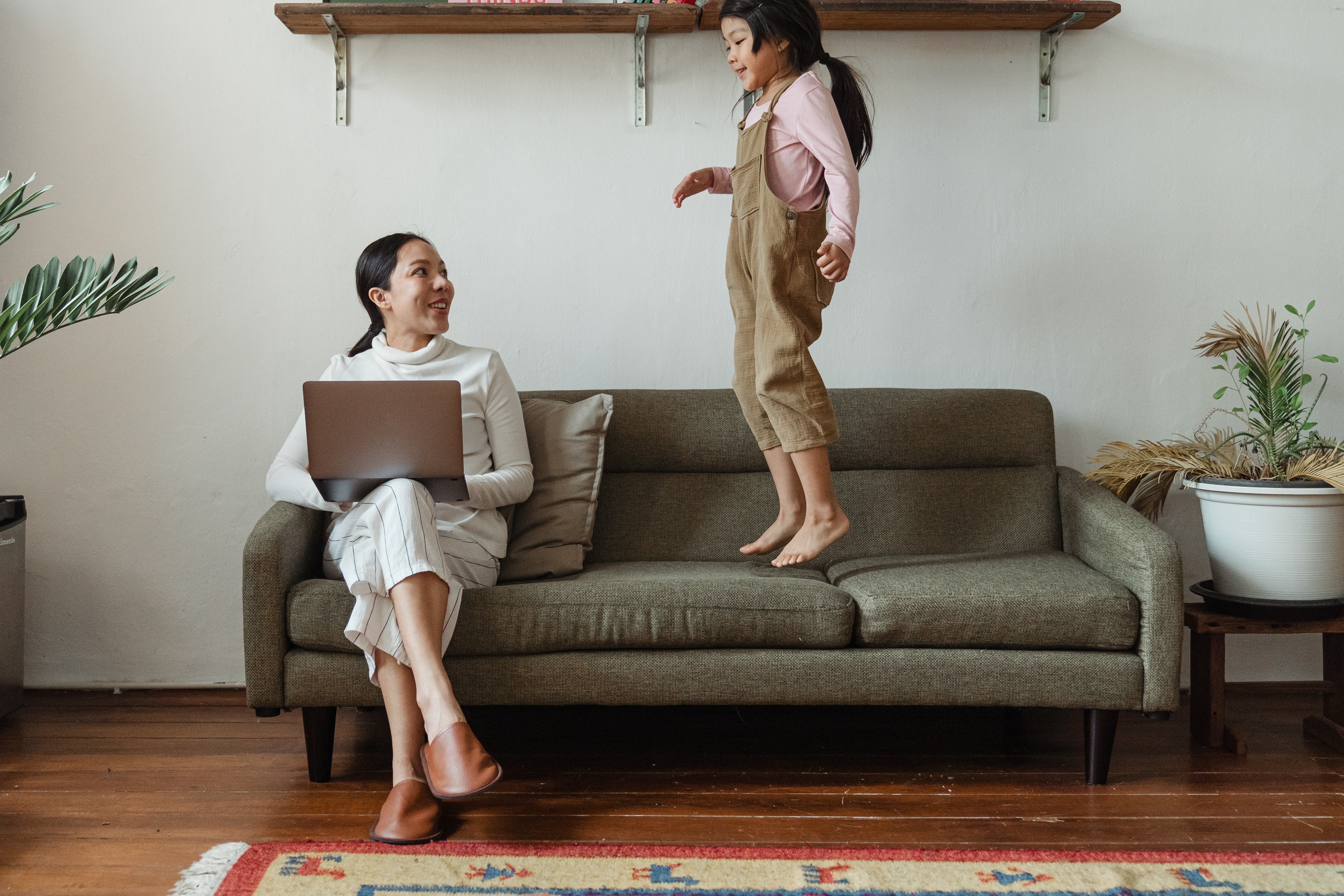 Cheerful woman with laptop and daughter on sofa