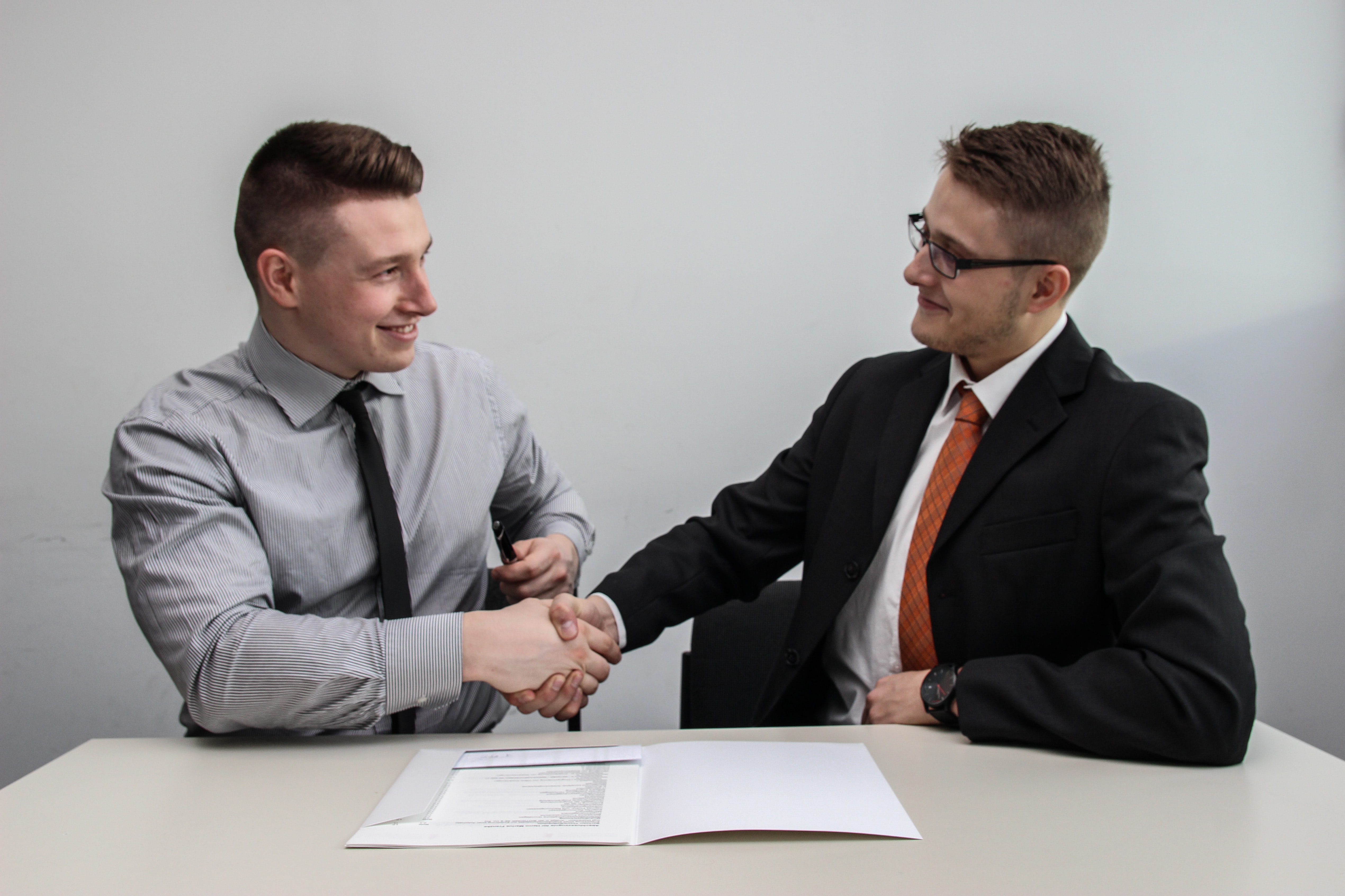 two employeesfacing each other while shake hands and smiling while reviewing employee benefits package