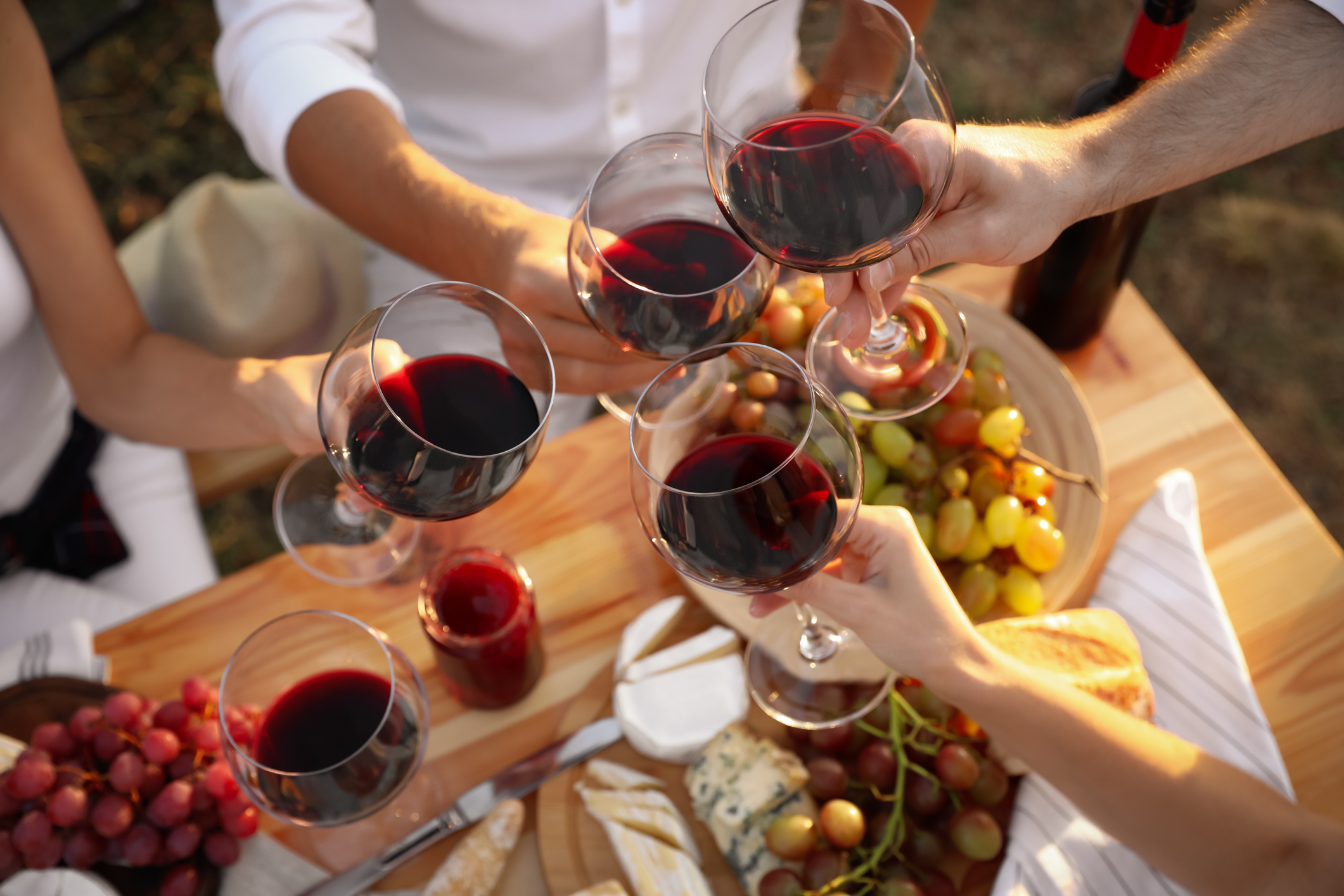 photo: wine glasses are raised over a wooden picnic table in evening light