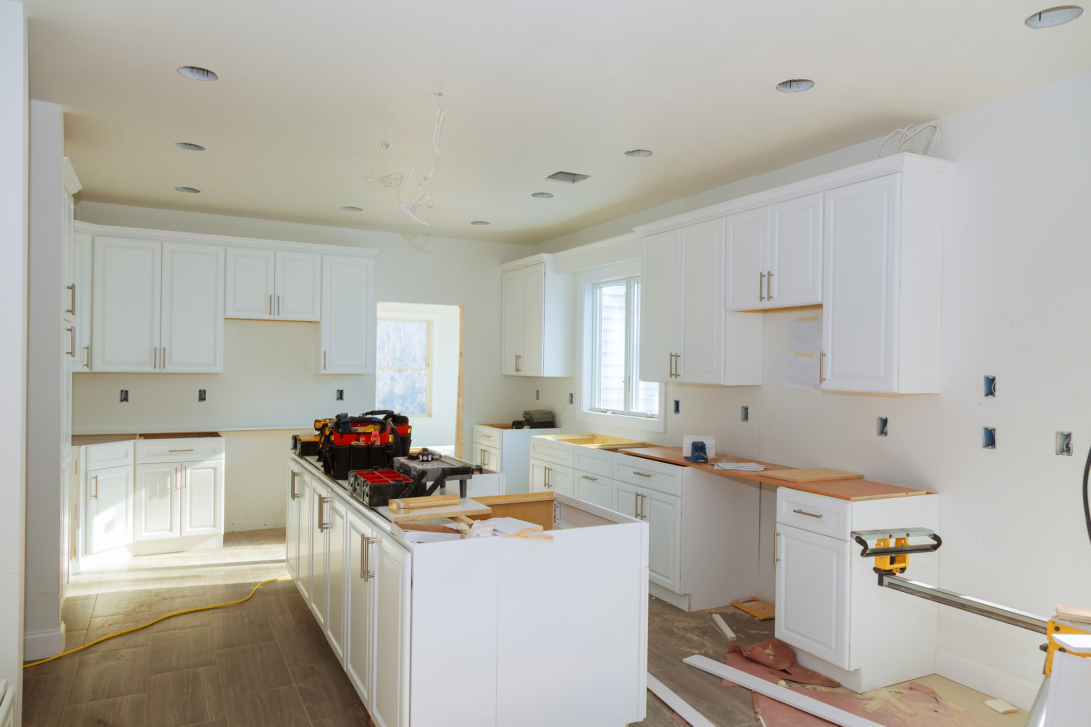 photo: a home kitchen under constuction with new cabinets partially installed. appliances, countertops, and other features are pending. tools and construction scraps are visible.