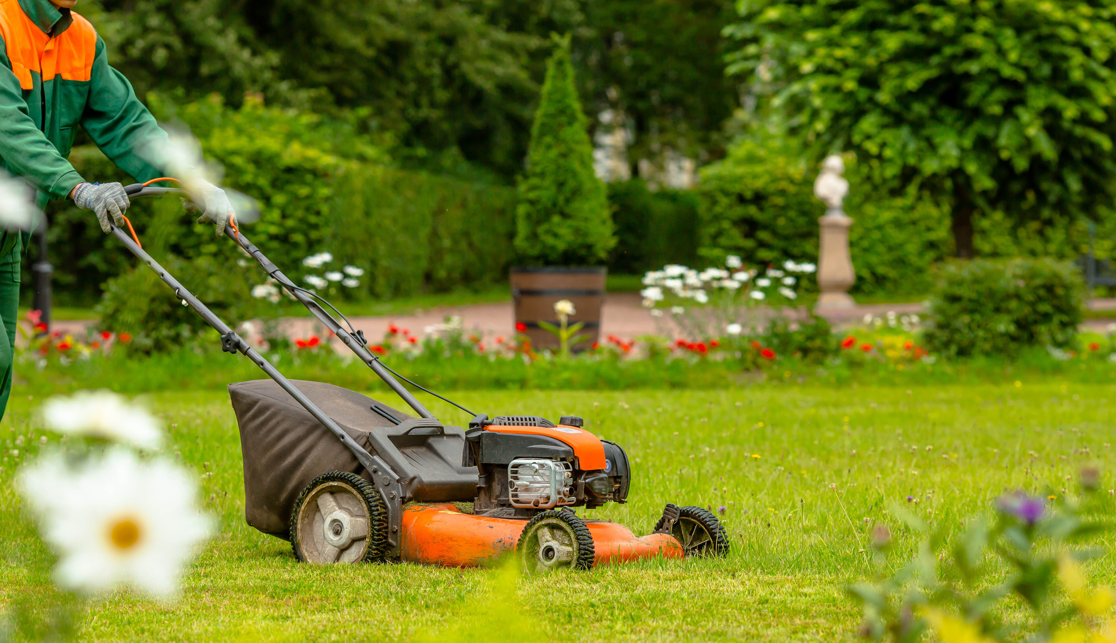 photo: a landscaper is shown mowing an upscale garden lawn bordered by wildflowers